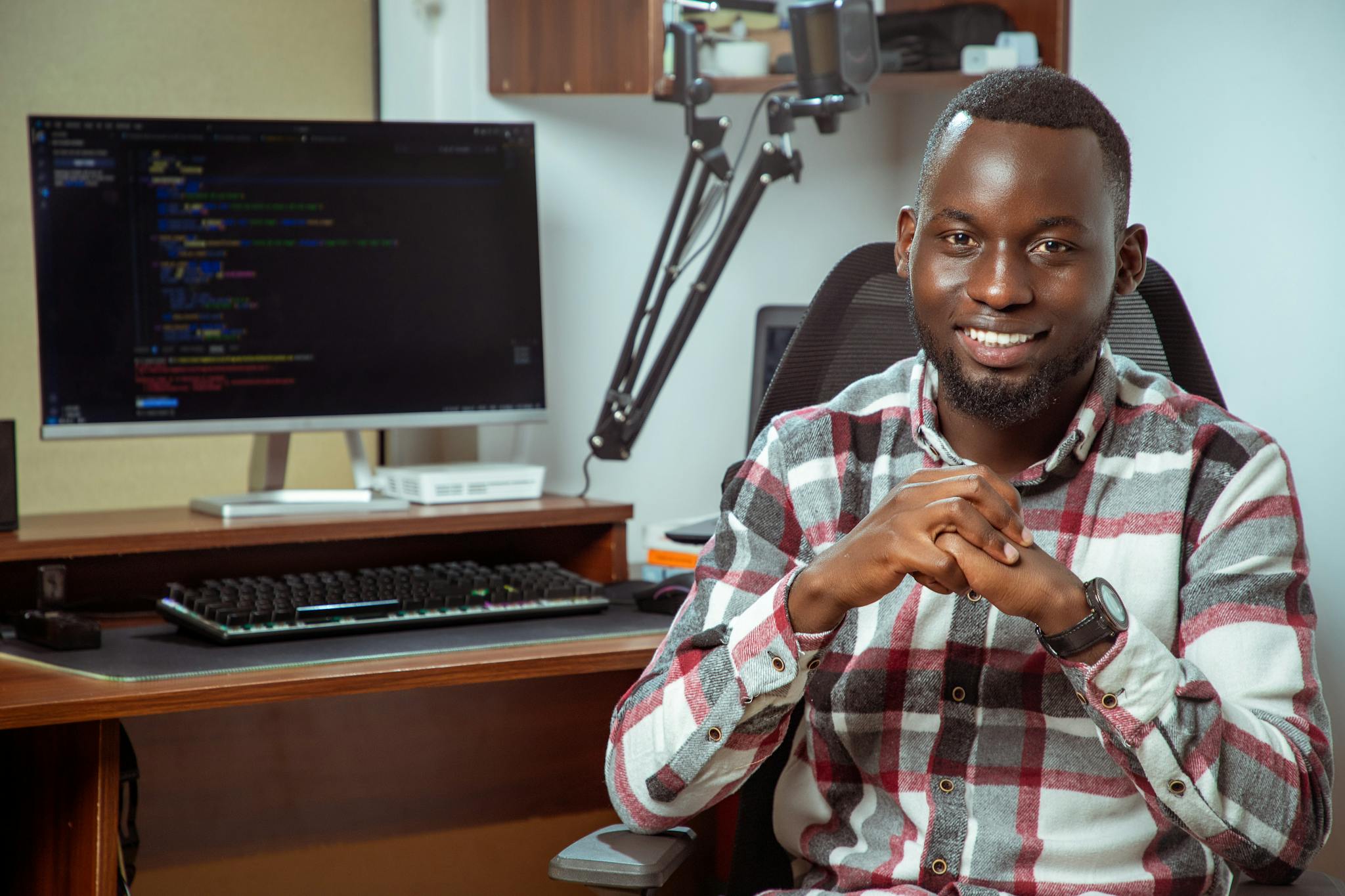 Portrait of a smiling programmer at a desk with computer screen displaying code.